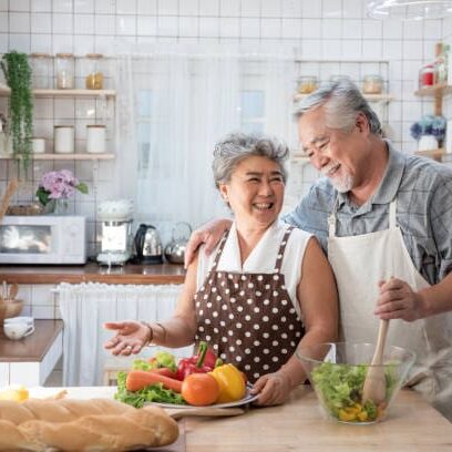 Senior couple having fun in kitchen with healthy food - Retired people cooking meal at home with man and woman preparing lunch with bio vegetables - Happy elderly concept with mature funny pensioner.